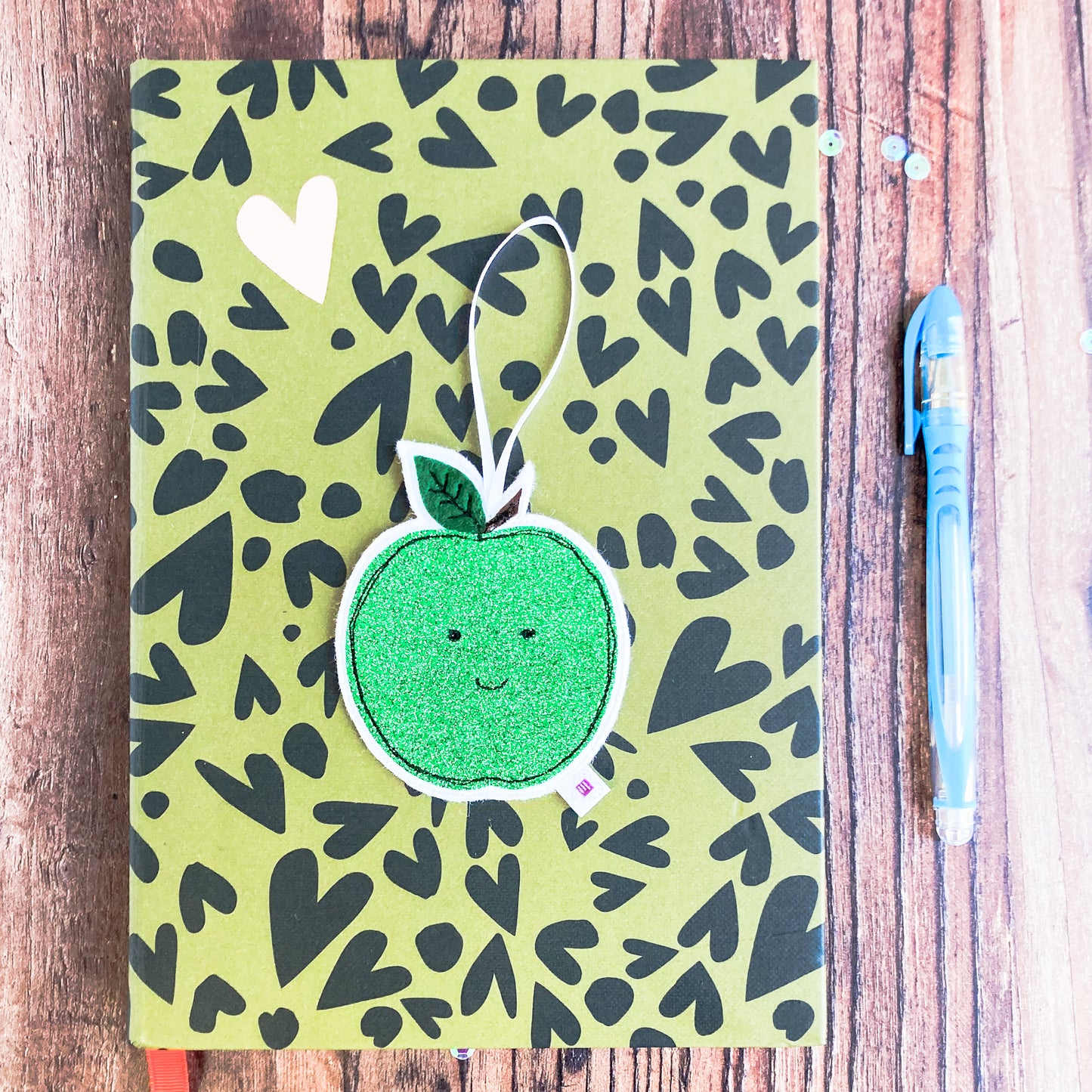 Green glittery apple decoration on a notebook with a pen and sequins 