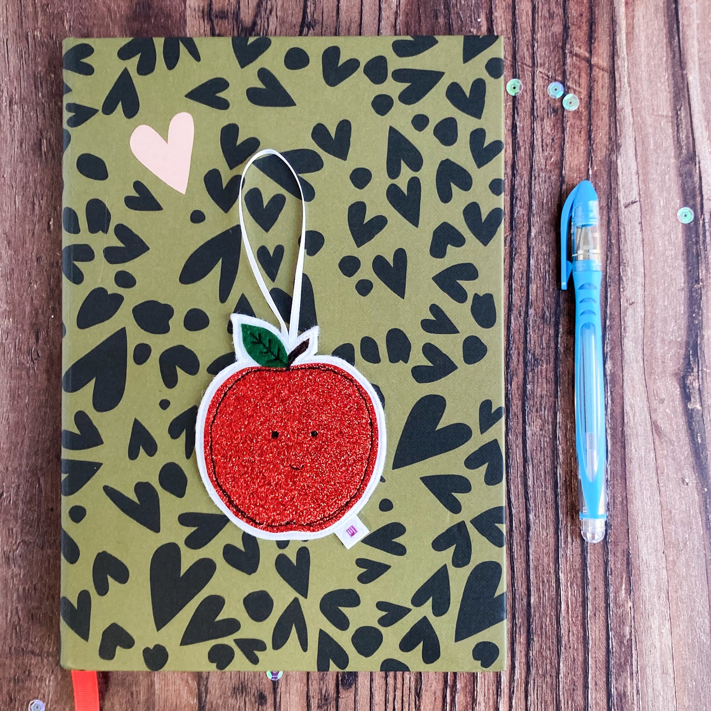 Red glittery apple decoration on a notebook with a pen and sequins 